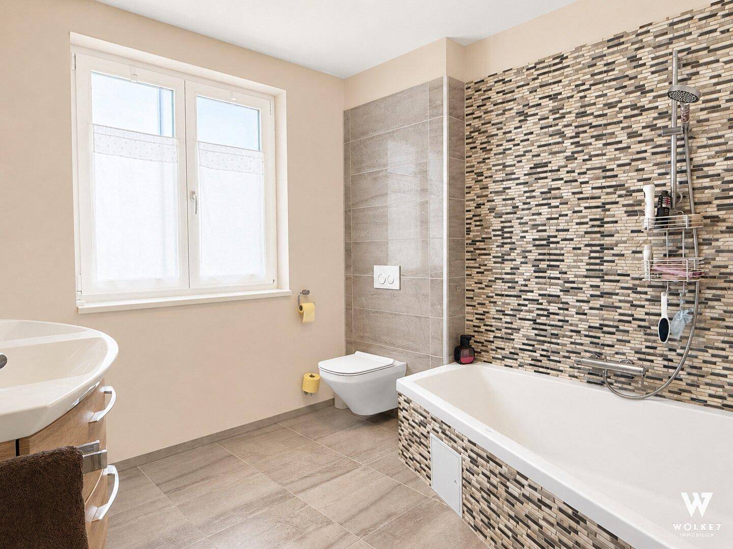 Modernes Badezimmer mit Badewanne, WC und Mosaikfliesen an der Wand.