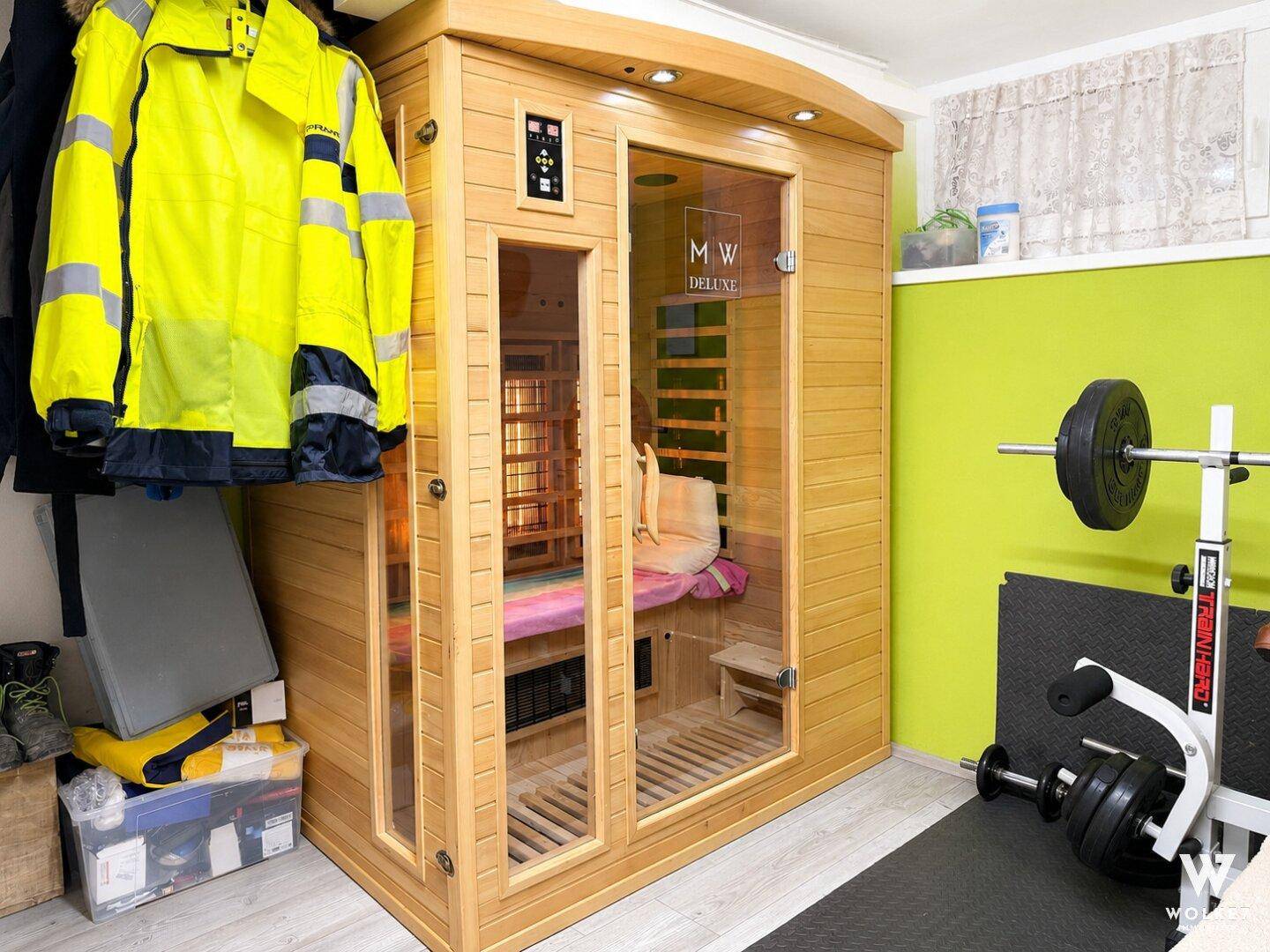 Detailansicht der modernen Infrarotsauna und des Fitnessbereichs mit Hanteln und Gewichten.