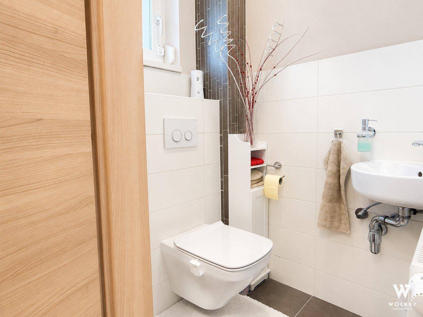 Modernes Gäste-WC mit wandhängendem WC, kleinem Waschbecken und Fenster für Tageslicht.
