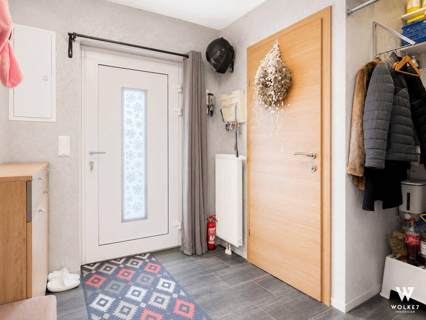 Heller Eingangsbereich mit moderner Haustür, Garderobe und dunklen Fliesen auf dem Boden.