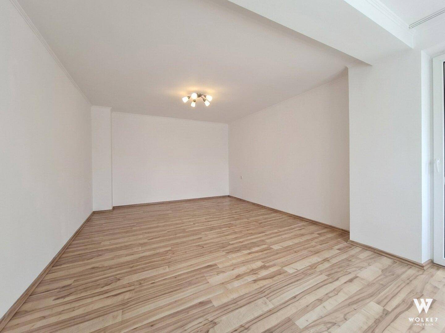 Heller, leerer Raum mit Laminatboden und weißen Wänden, bereit zur individuellen Gestaltung.