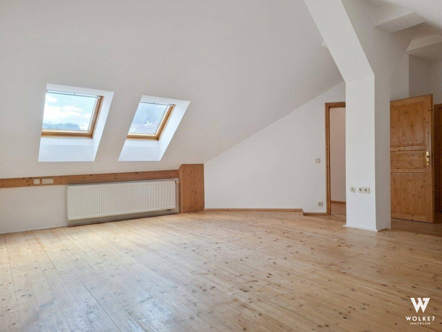 Helles Dachzimmer mit Holzboden, Dachfenstern und schrägen Wänden, bietet vielseitige Nutzungsmöglichkeiten.