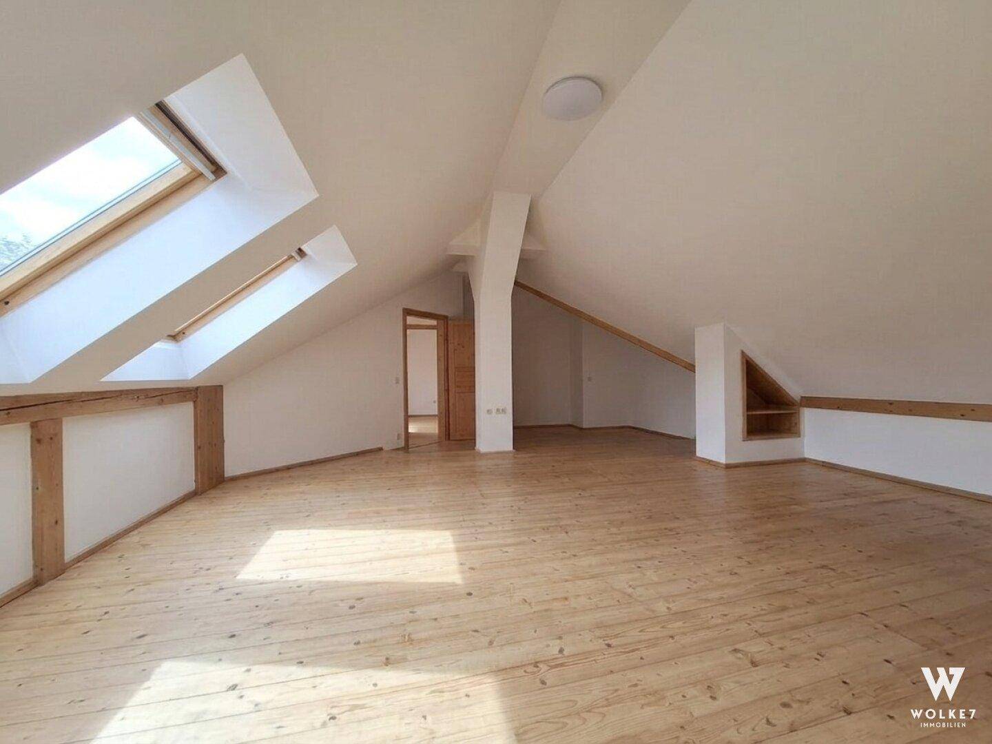 Geräumiges Dachzimmer mit Holzboden, Dachfenstern und sichtbaren Holzbalken.