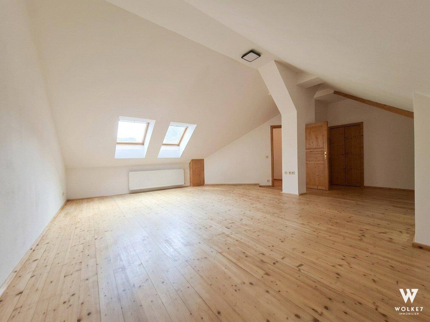 Helles Dachzimmer mit Holzboden, Dachfenstern und integrierten Holzschränken.