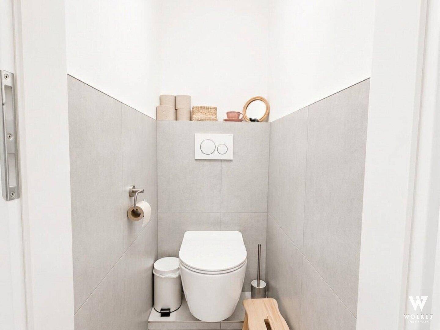Modernes Gäste-WC mit hellgrauen Fliesen, wandhängendem WC und minimalistischer Dekoration.
