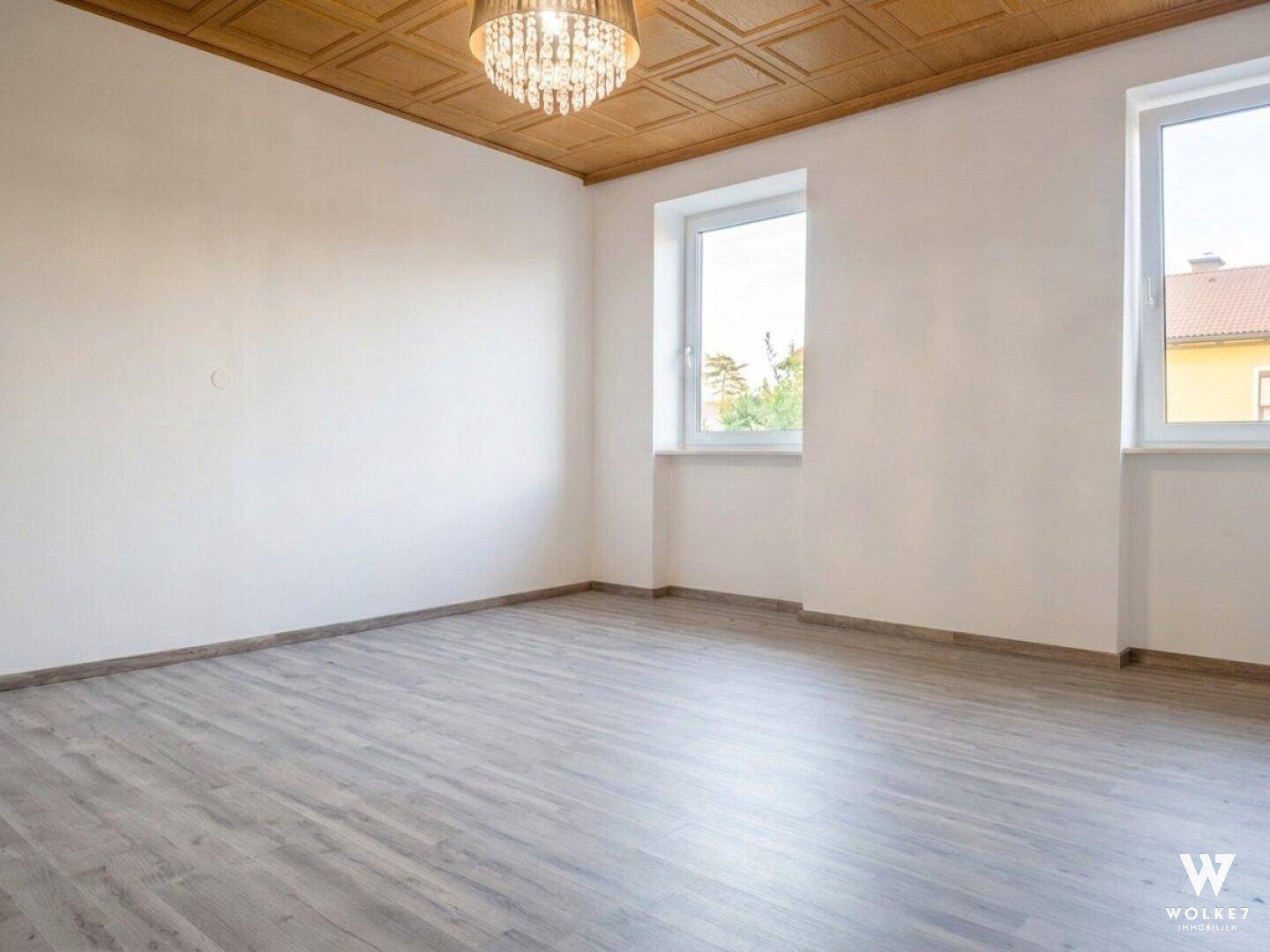 Geräumiges Zimmer mit Holzkassettendecke, Laminatboden und zwei Fenstern.