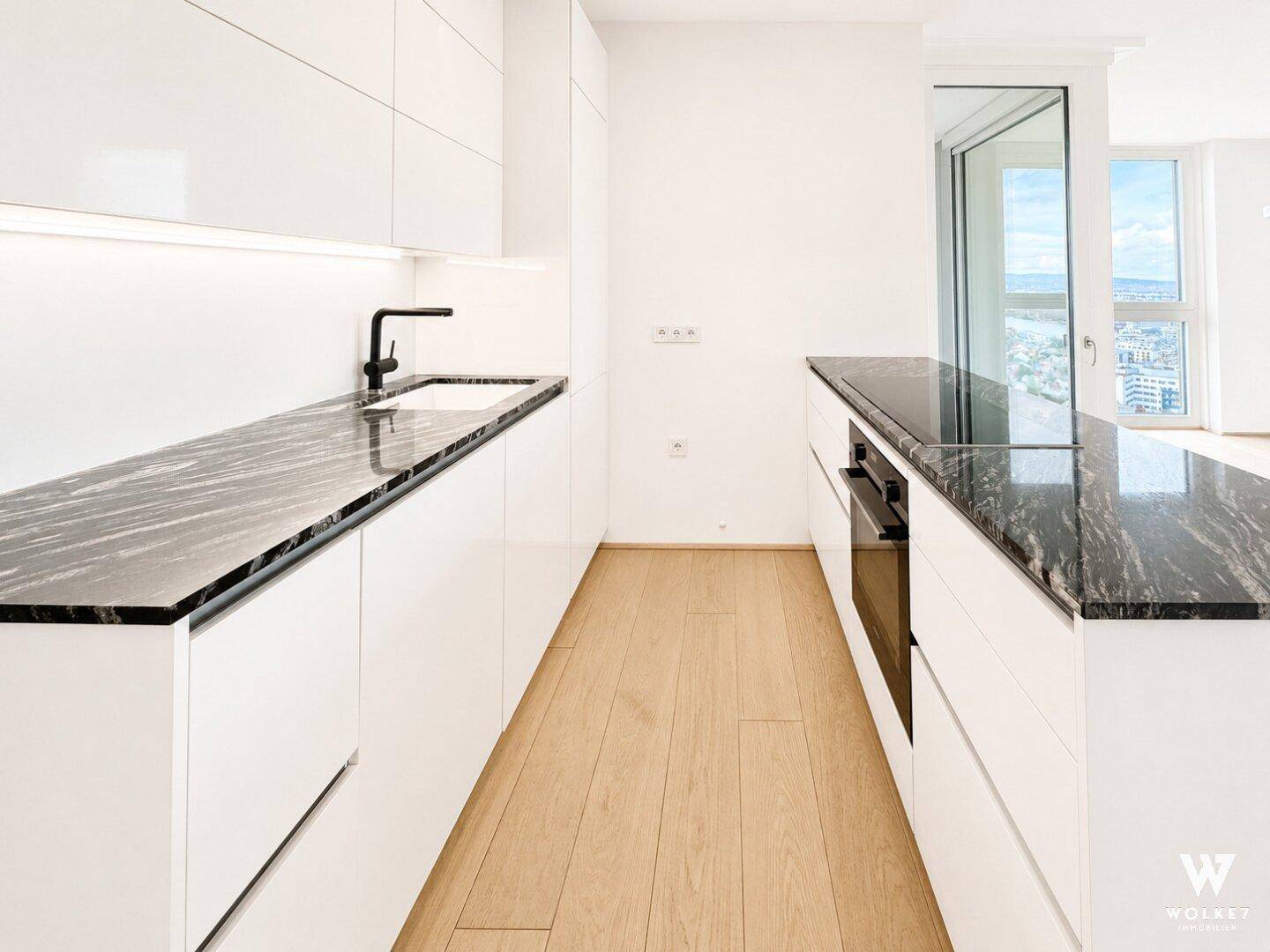 Elegante weiße Küche mit langen Granitarbeitsplatten, Holzboden und viel Stauraum.