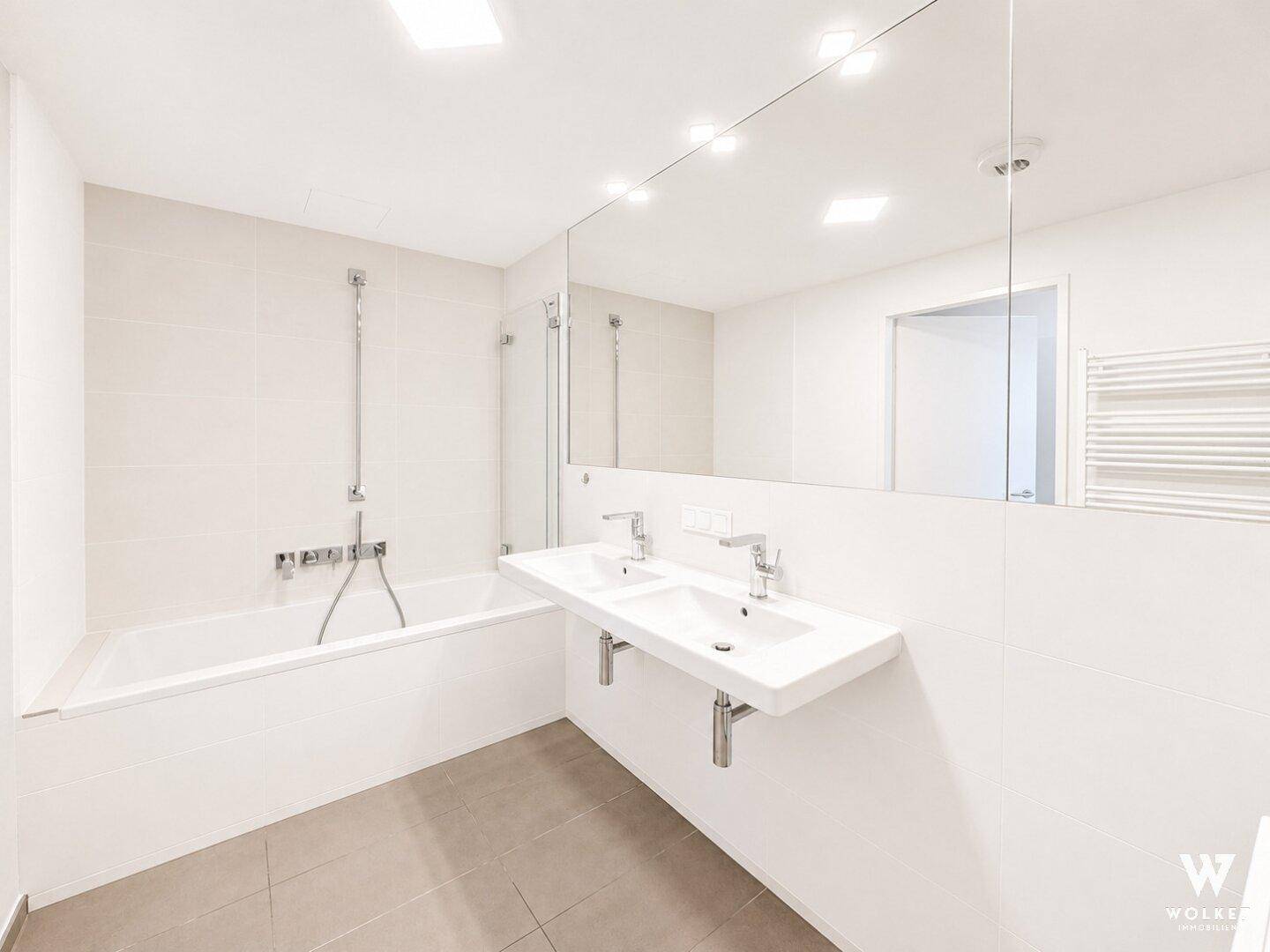 Modernes Badezimmer mit Badewanne, Doppelwaschbecken und großem Spiegel in hellen Fliesen.