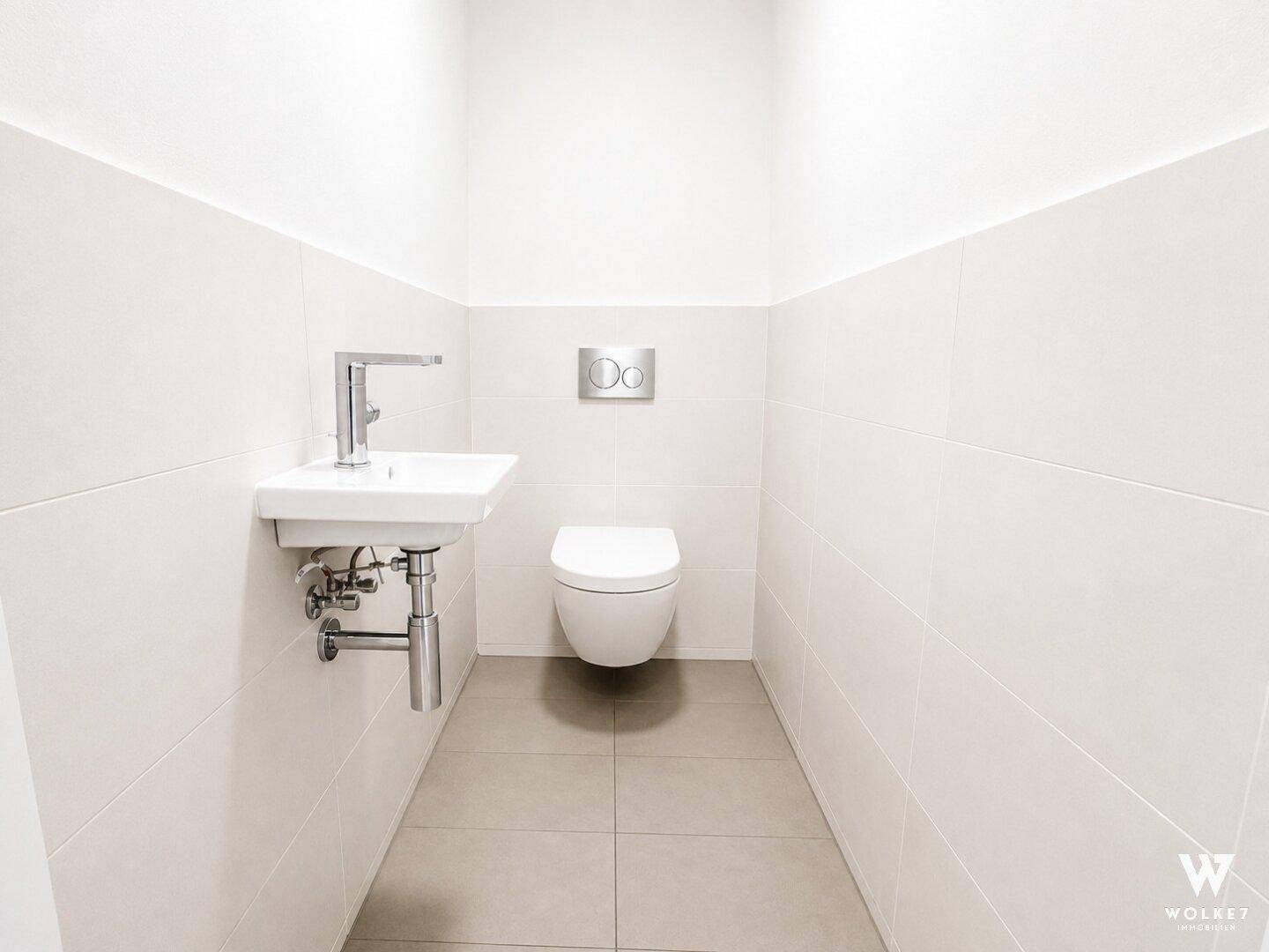 Modernes Gäste-WC mit wandhängender Toilette, kleinem Waschbecken und hellen Fliesen.