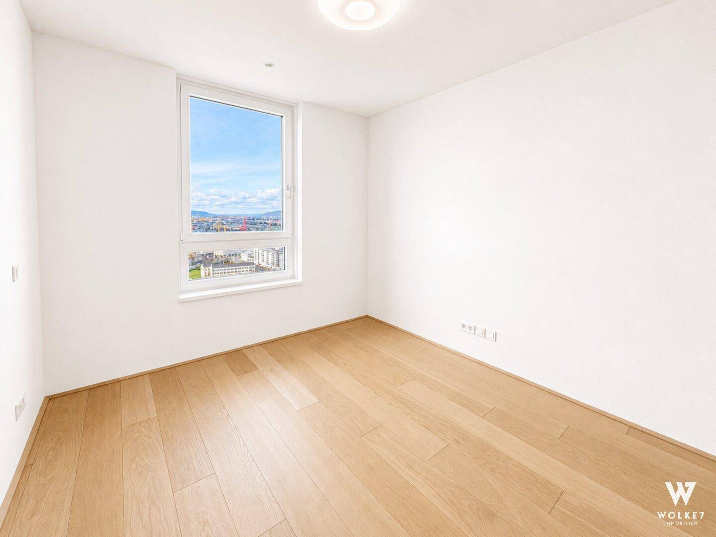 Geräumiges, helles Schlafzimmer mit Holzboden, großem Fenster und Panoramablick auf die Stadt.