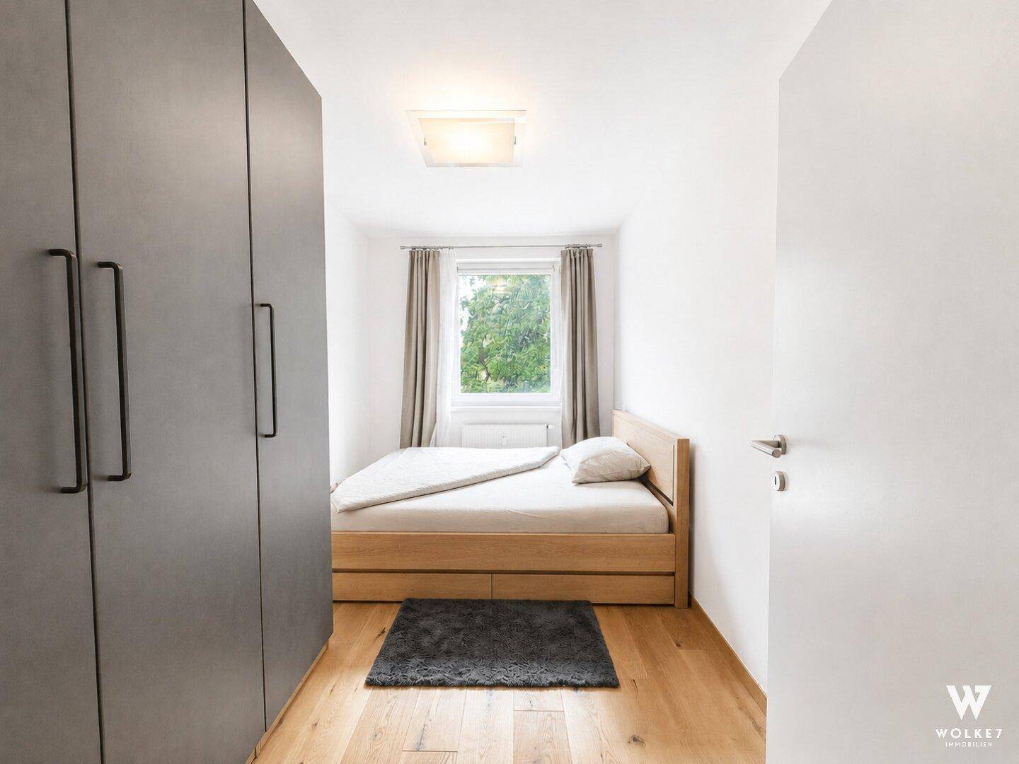 Gemütliches Schlafzimmer mit Holzbett, großem Kleiderschrank und Fenster mit Grünblick.