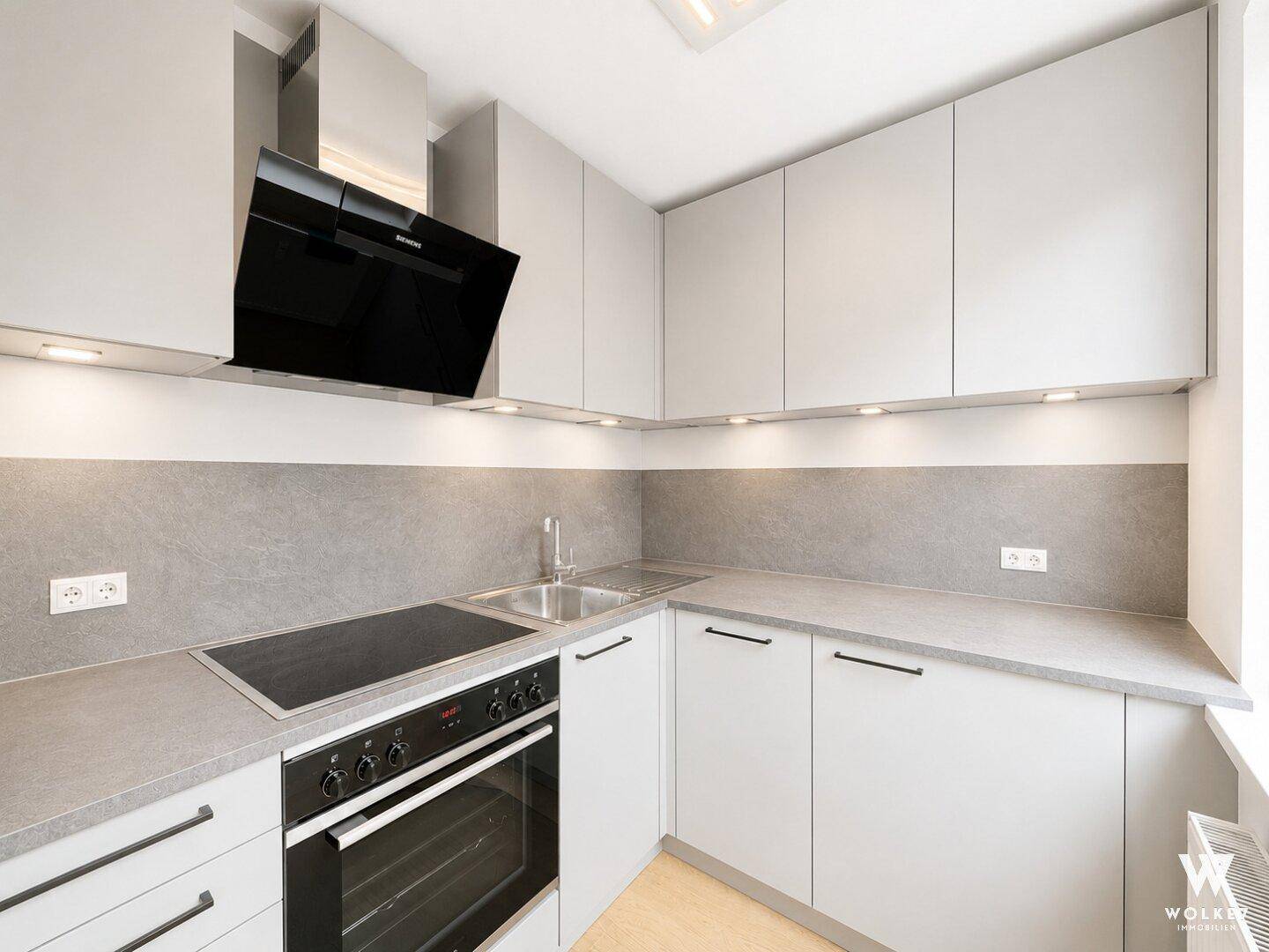 Moderne Einbauküche in Grau mit Induktionskochfeld, Backofen und Dunstabzugshaube.