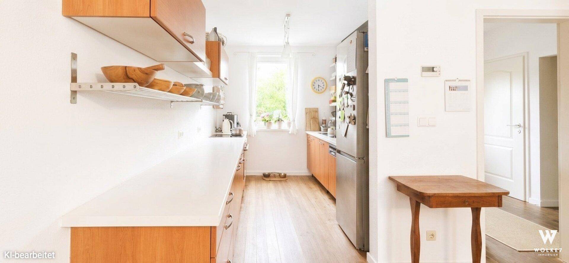 Helle Küche mit Holzschränken, weißen Arbeitsplatten und Fenster mit Blick ins Grüne.