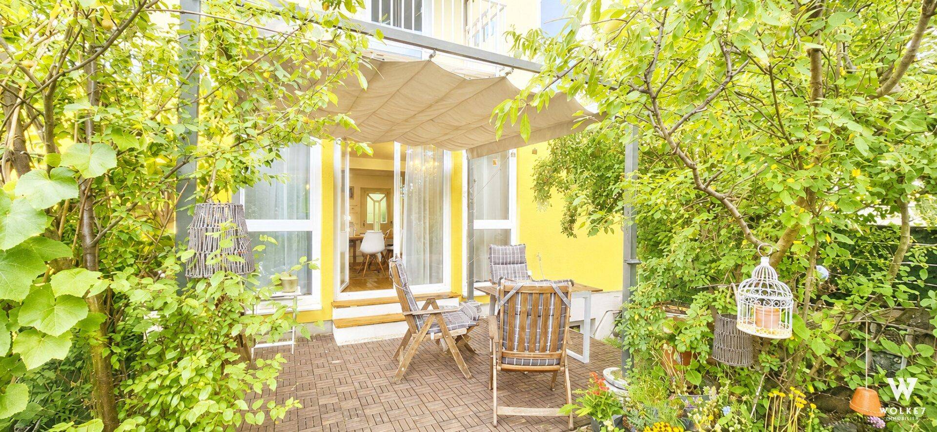 Gemütliche Terrasse mit Gartenmöbeln und Sonnenschutz, umgeben von üppigem Grün.