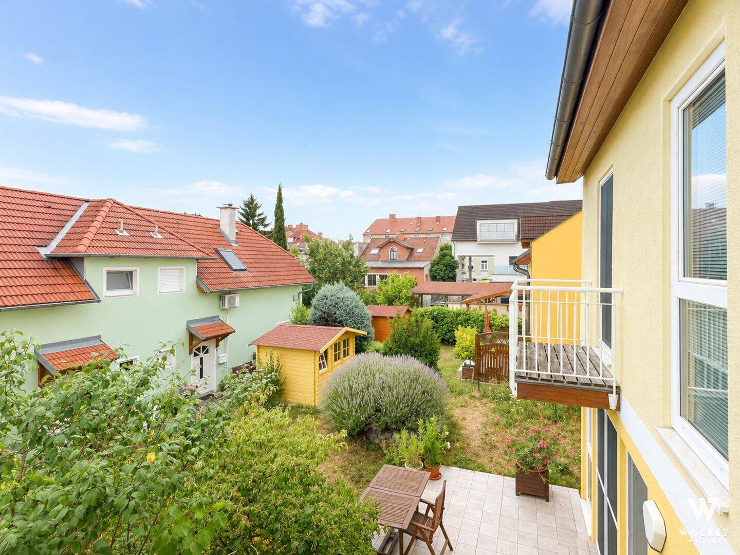 Blick über den Garten mit Gartenhäuschen und einem kleinen Balkon am Haus.