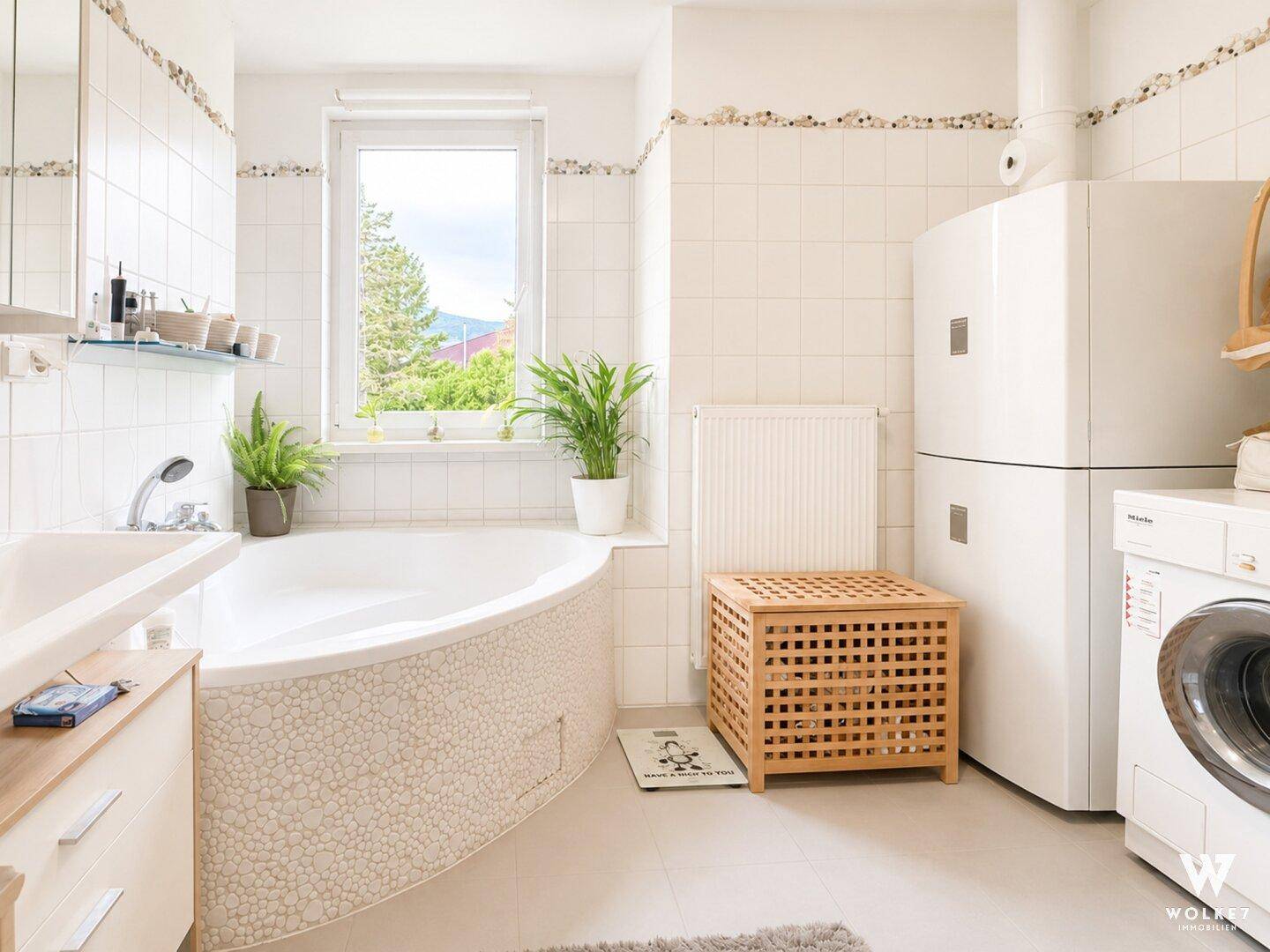 Helles Badezimmer mit Eckbadewanne, Fenster und Waschmaschine.