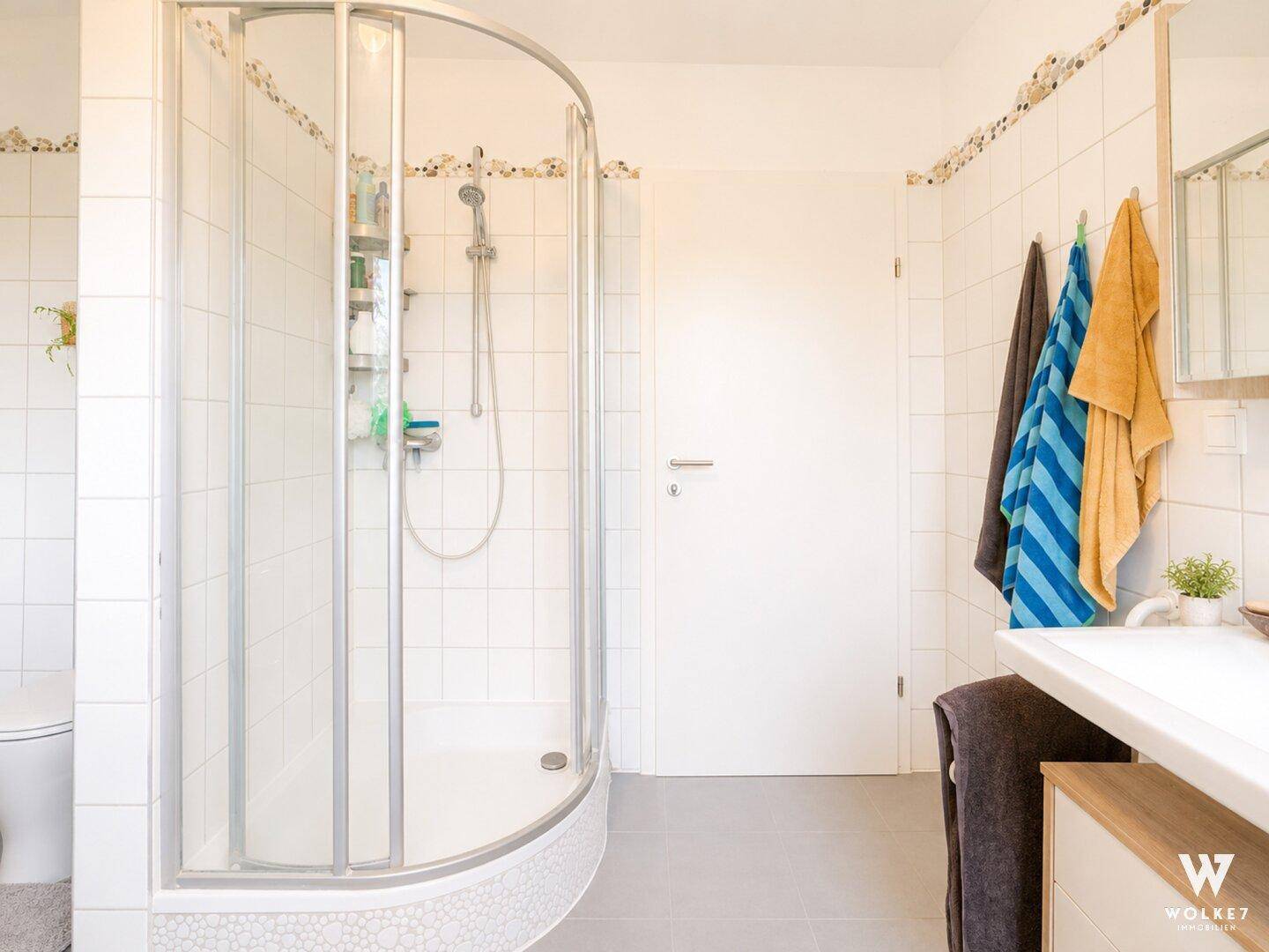 Modernes Badezimmer mit Duschkabine, weißen Fliesen und Handtuchhalter.