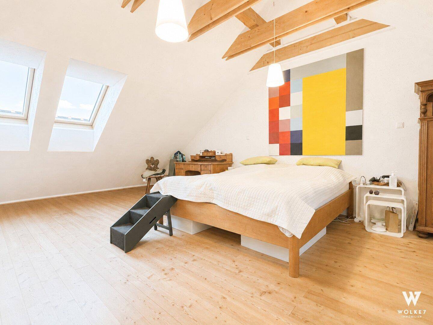Geräumiges Schlafzimmer im Dachgeschoss mit Holzbalken, Dachfenstern und Holzboden.