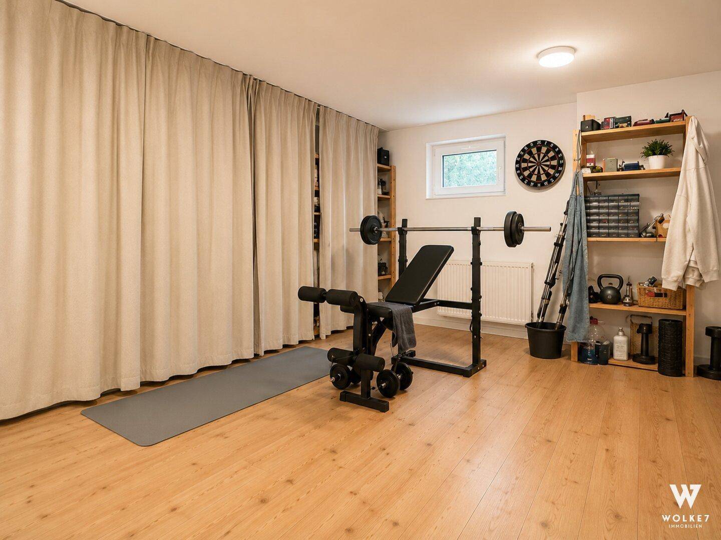 Heim-Fitnessraum mit Holzboden, Hantelbank und Regalen für Sportgeräte.