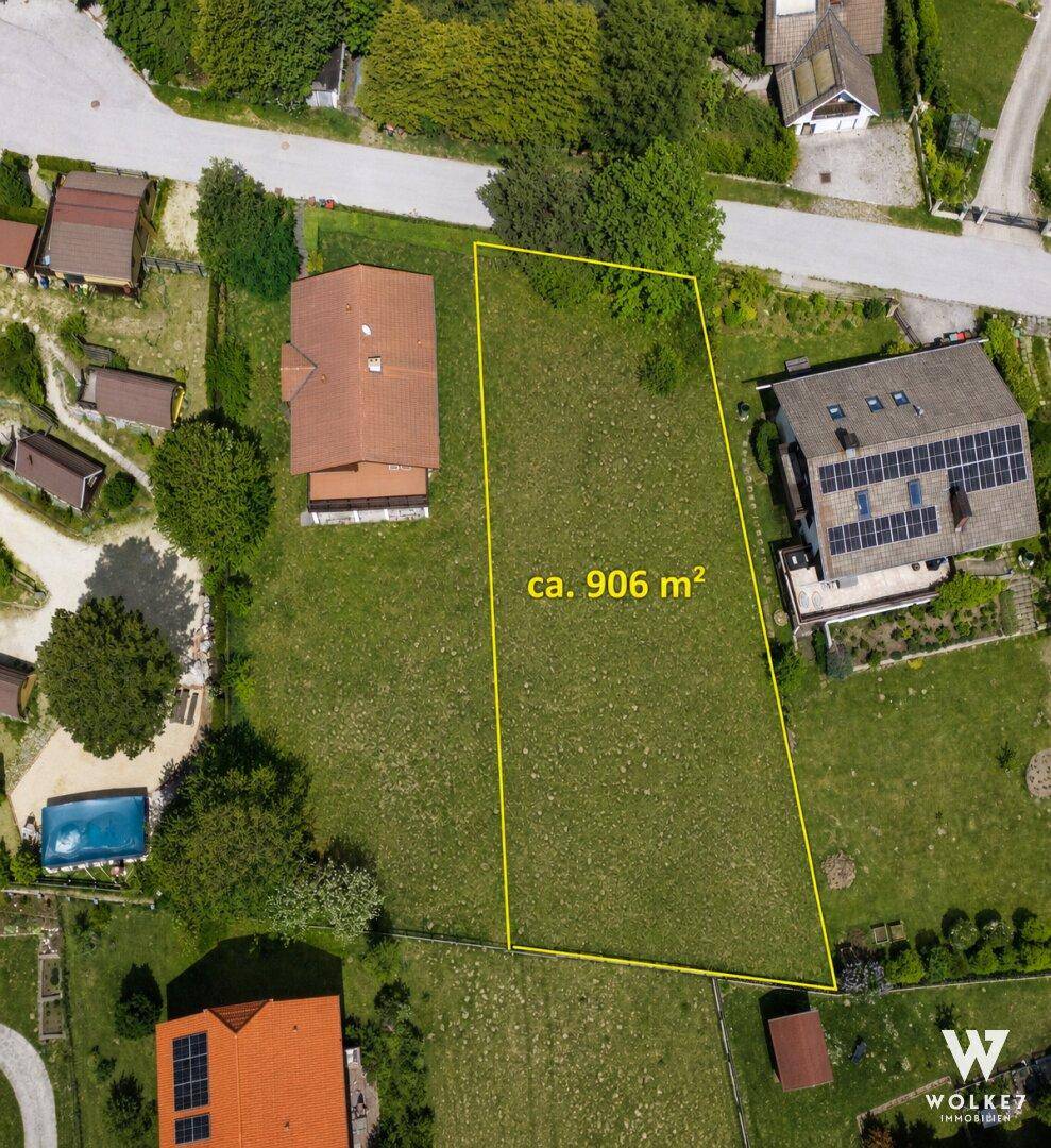 Übersichtliche Luftaufnahme eines Baugrundstücks von ca. 906 m² mit umliegenden Häusern und Vegetation.