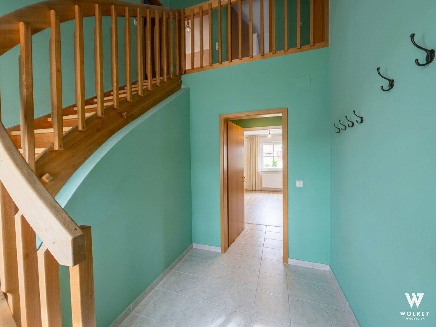 Heller Flur mit Holztreppe und mintgrünen Wänden, führt zu weiteren Räumen.