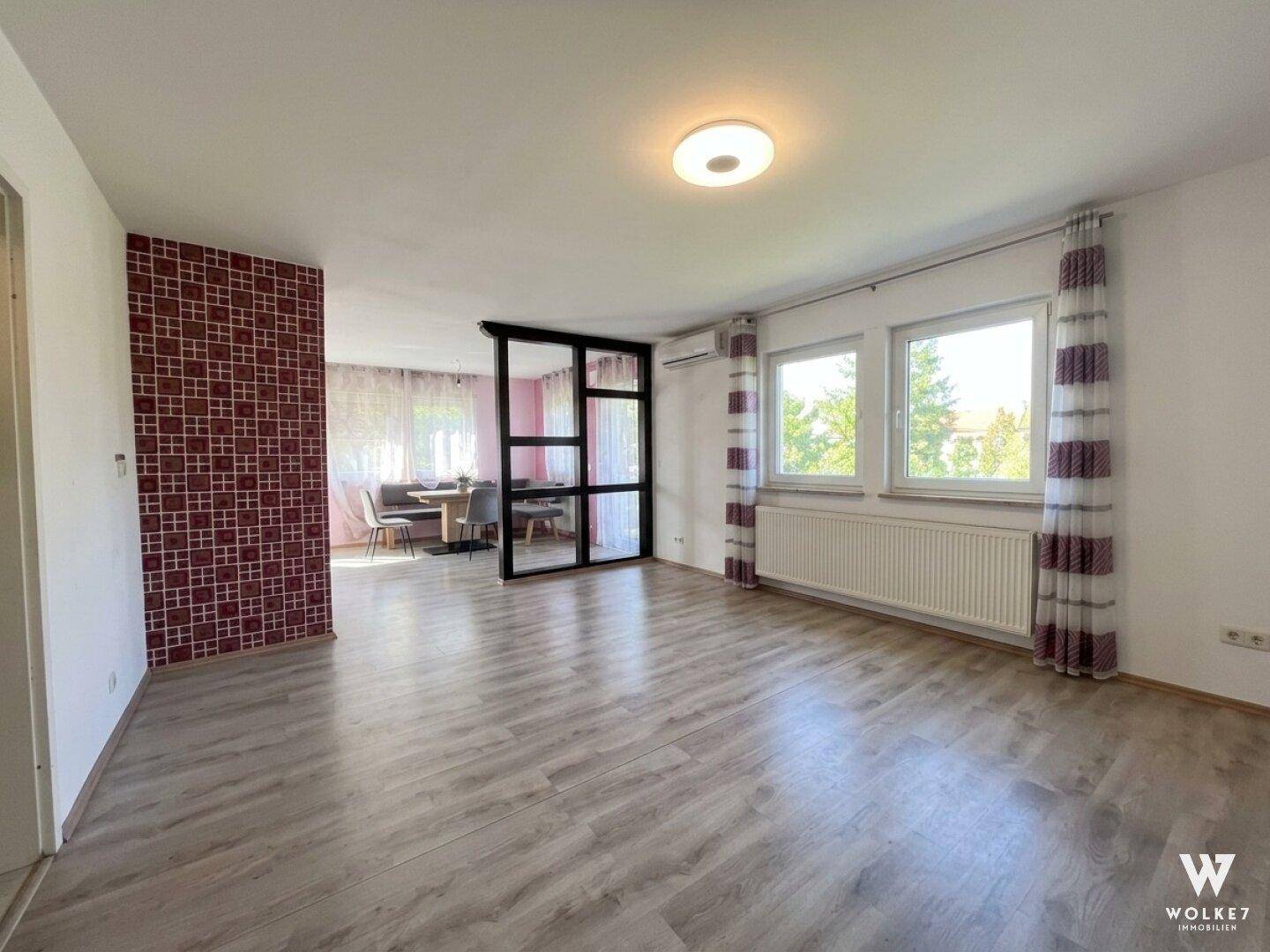 Geräumiger Wohnbereich mit Laminatboden, großen Fenstern und angrenzendem Essbereich.