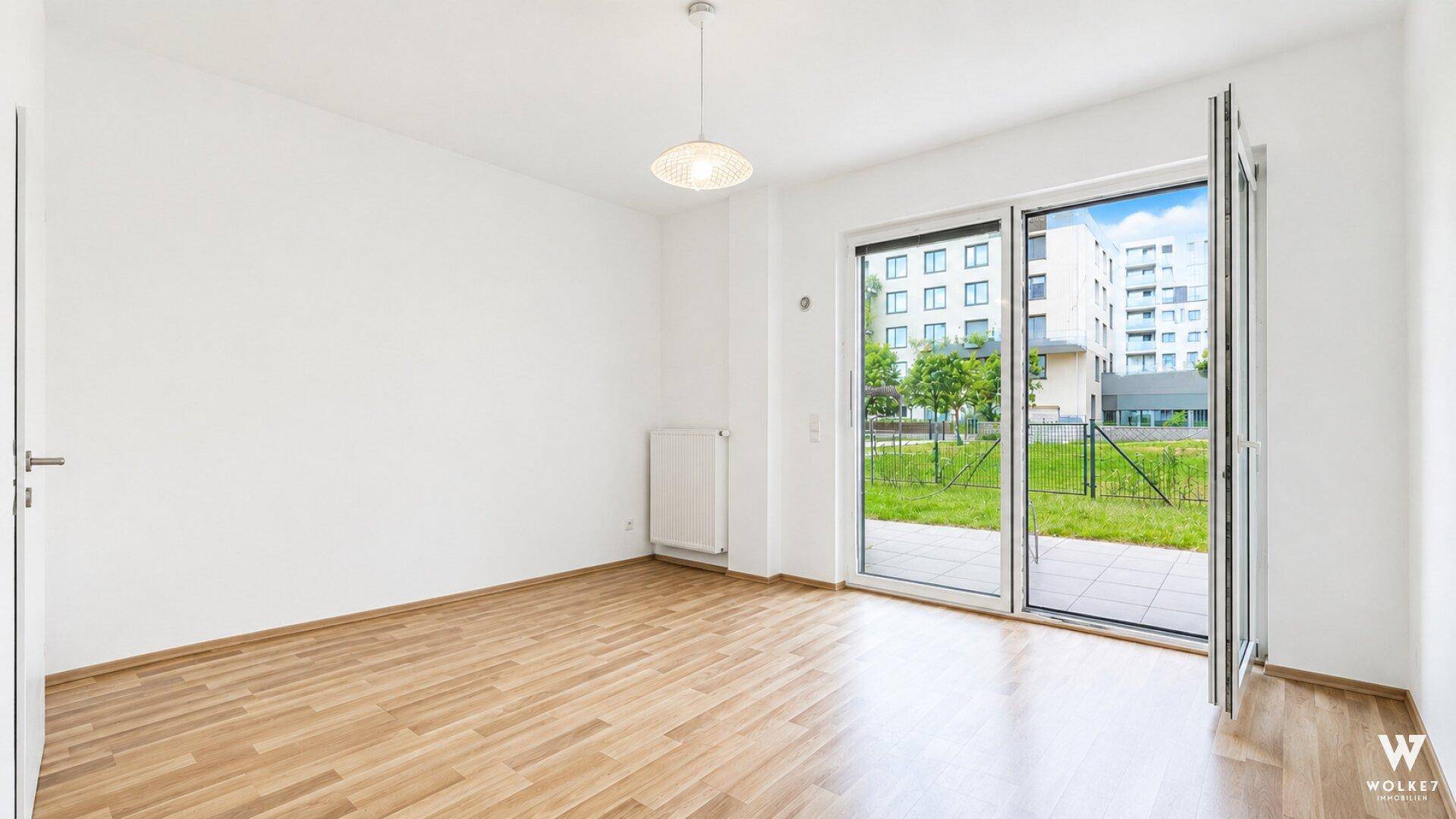 Helles, leeres Zimmer mit Parkettboden und großen Fenstern zum Außenbereich.