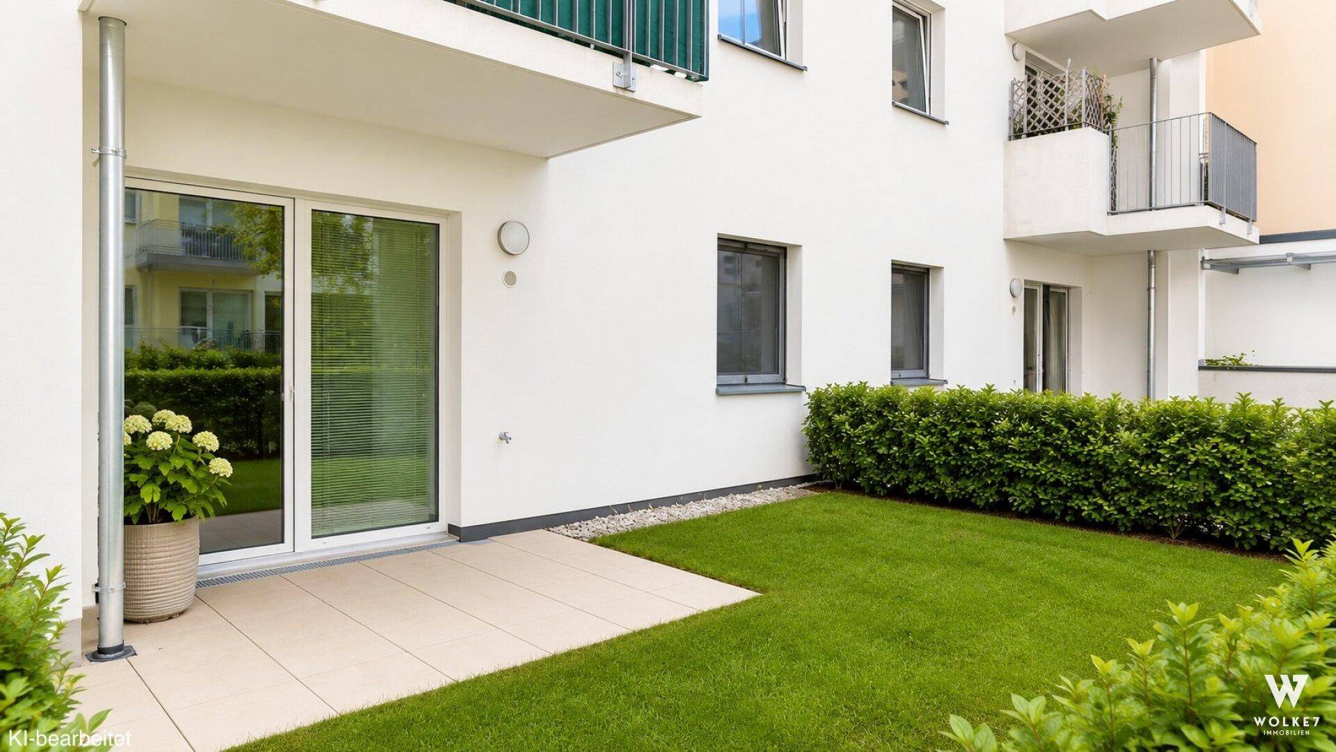 Eine gepflegte Terrasse mit direktem Zugang zum Rasen und grünen Büschen.