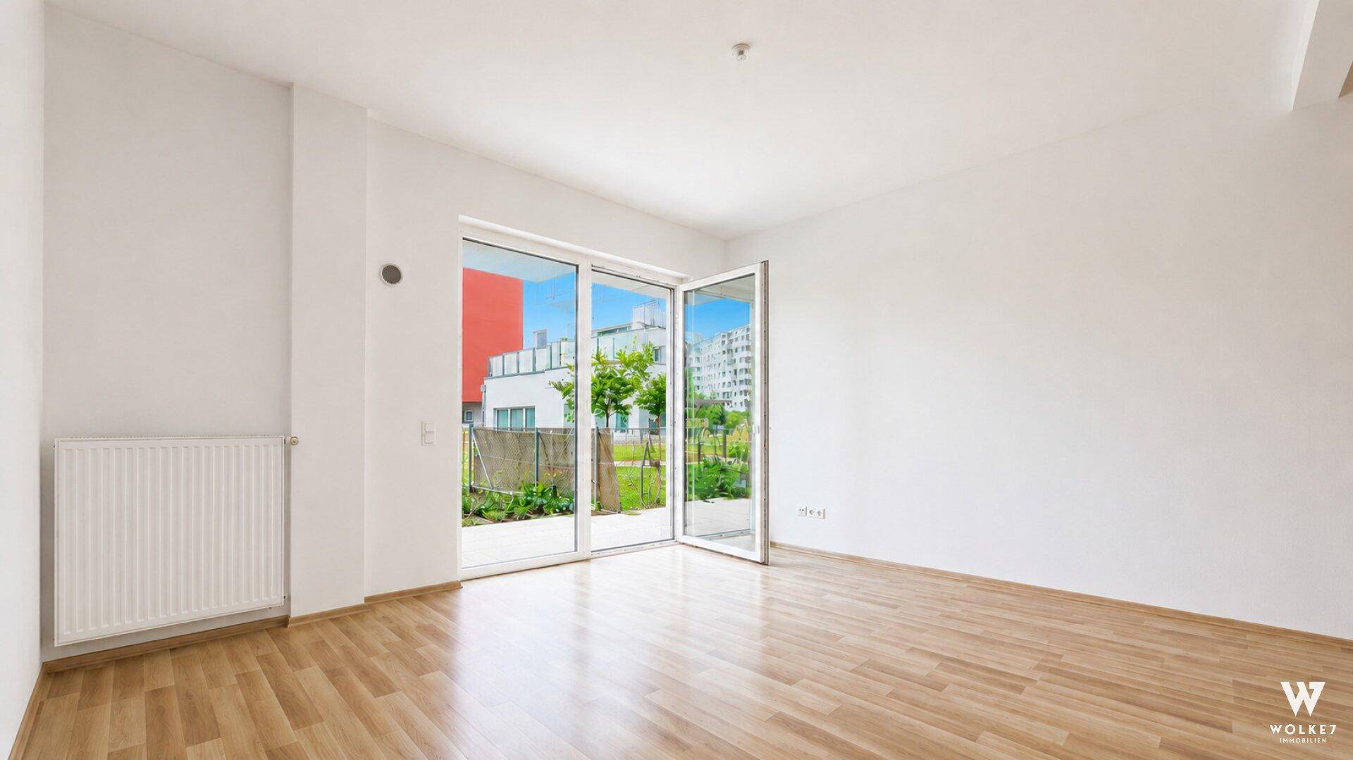 Geräumiges, helles Zimmer mit Holzboden und Zugang zu einem Außenbereich.