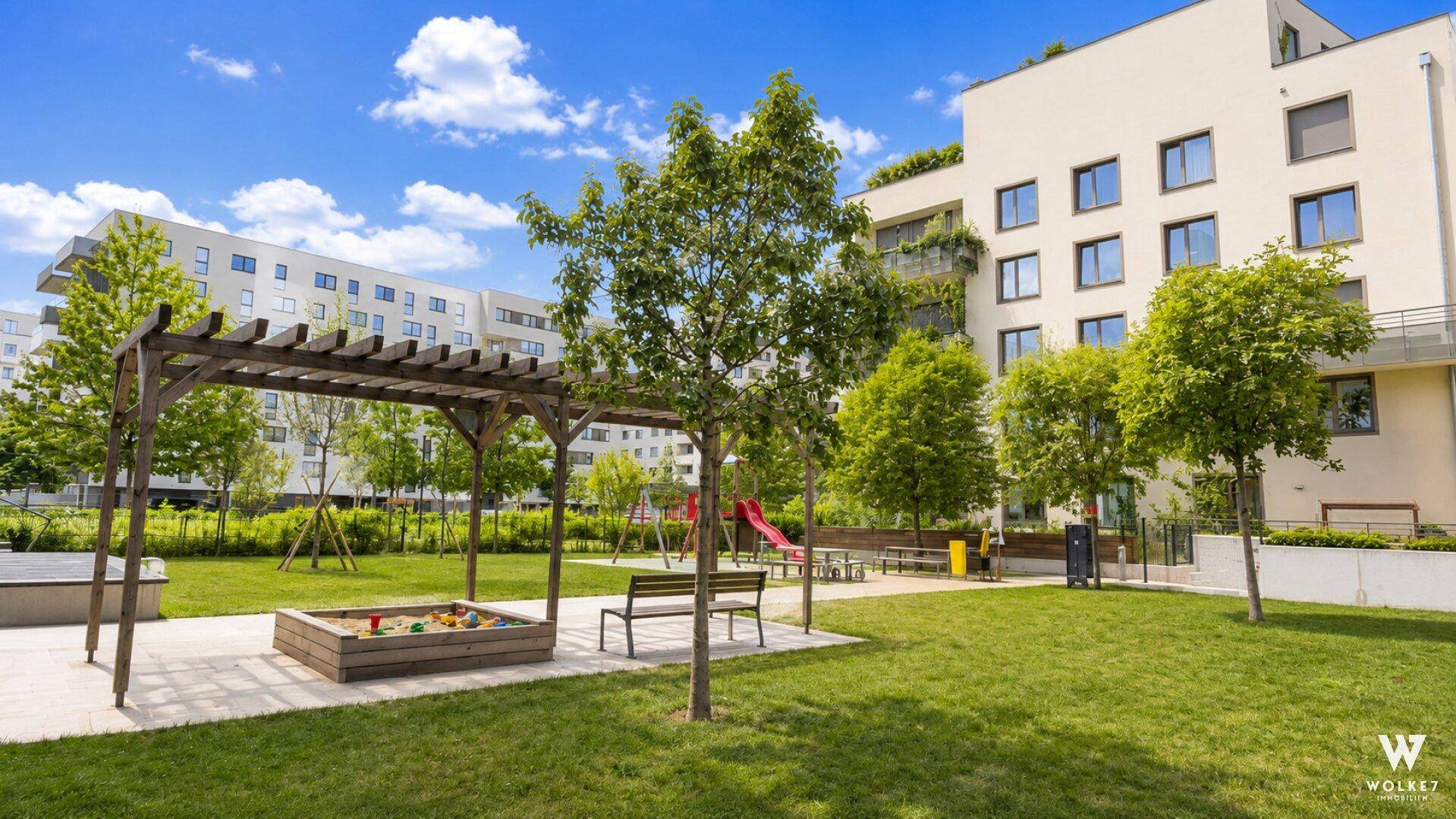Großer Gemeinschaftsgarten mit Spielplatz, Bänken und vielen Bäumen für Erholung.