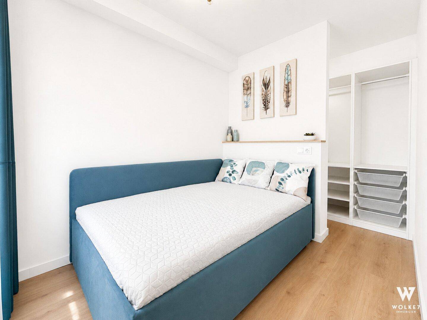 Helles Schlafzimmer mit Bett, Holzboden und offenem Kleiderschrankbereich, modern gestaltet.