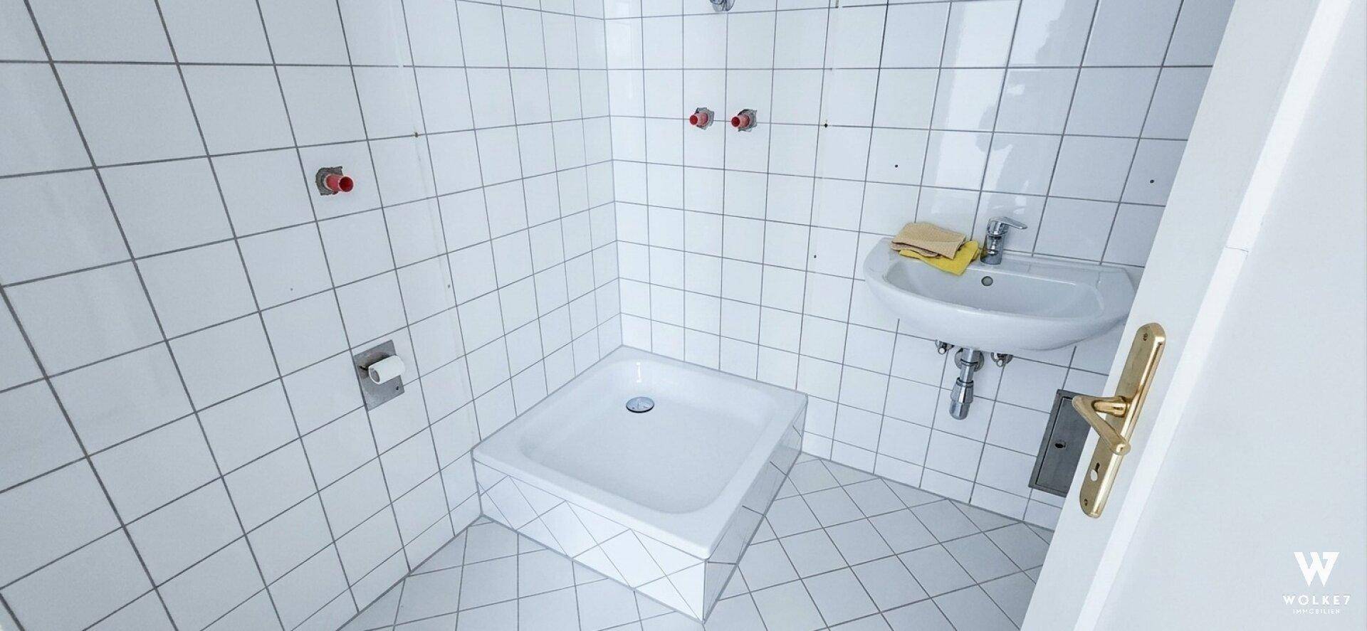 Badezimmer in Renovierung mit weißen Fliesen, Duschwanne und Waschbecken.