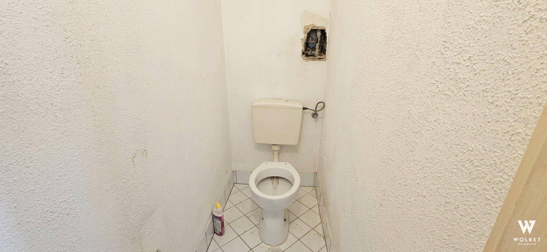 Kleines WC mit alter Toilette und Fliesenboden, bereit für eine Renovierung.