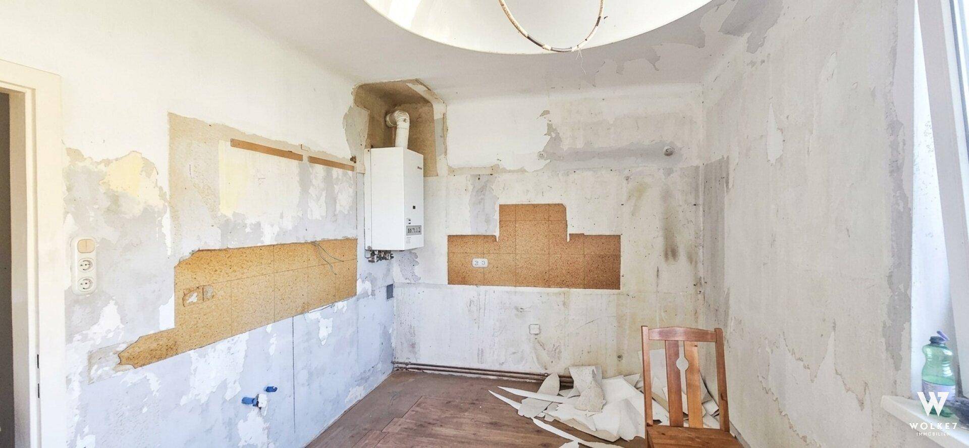 Raum in Renovierung mit freigelegten Wänden und sichtbarem Warmwasserbereiter.