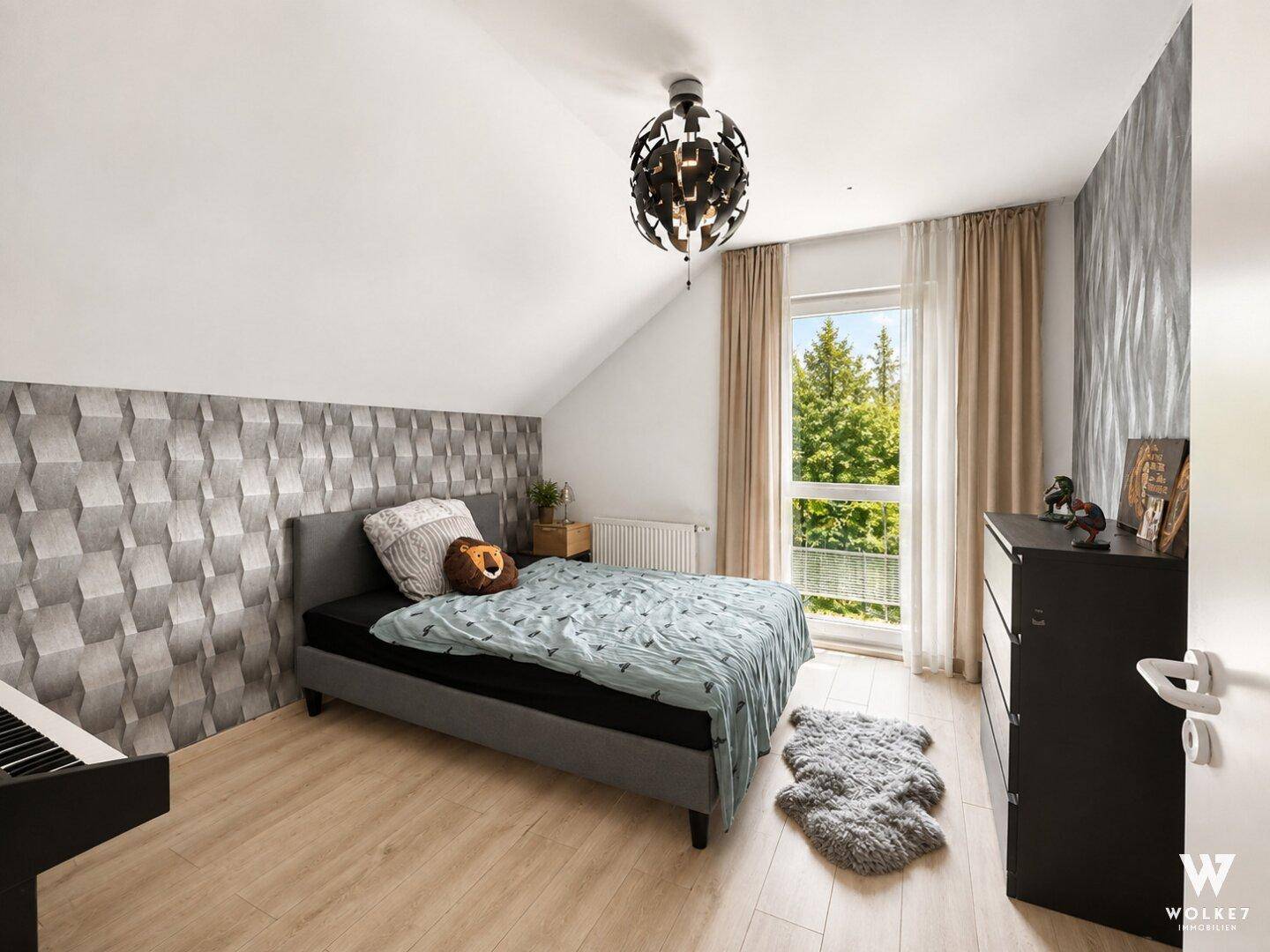 Helles Schlafzimmer mit Dachschräge, Einzelbett und einem Fenster mit Blick ins Grüne.