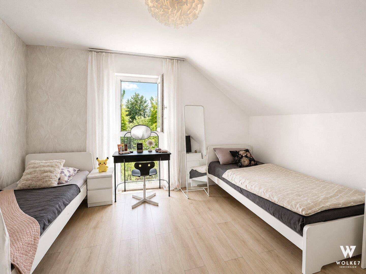 Kinderzimmer mit zwei Einzelbetten, Dachschräge und einem Fenster, das viel Tageslicht hereinlässt.