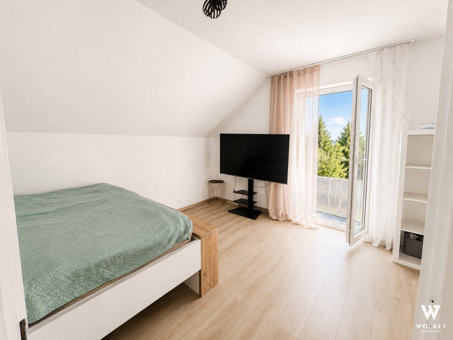 Schlafzimmer mit Doppelbett, Dachschräge und Zugang zu einem französischen Balkon mit Ausblick.