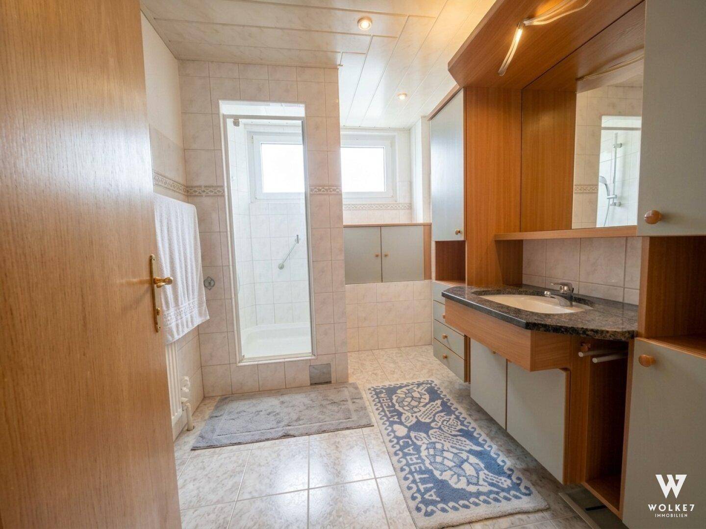 Badezimmer mit Dusche, Einzelwaschbecken und hellen Fliesen.