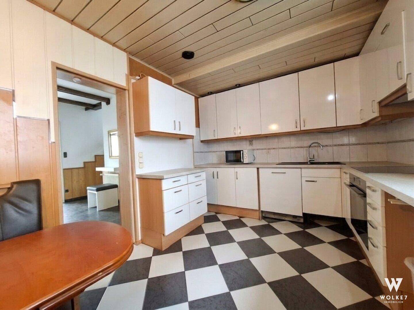 Küche mit weißen Schränken, kariertem Fliesenboden und Holzdeckenverkleidung.