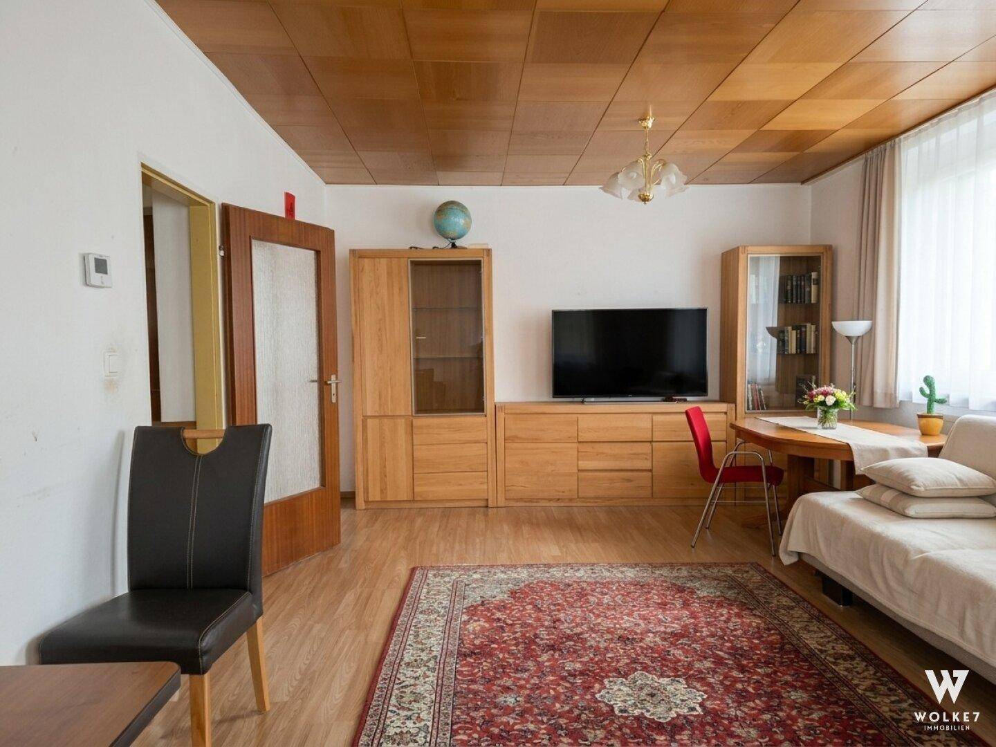 Wohn-Essbereich mit Holzmöbeln, Teppich und Holzdeckenverkleidung.