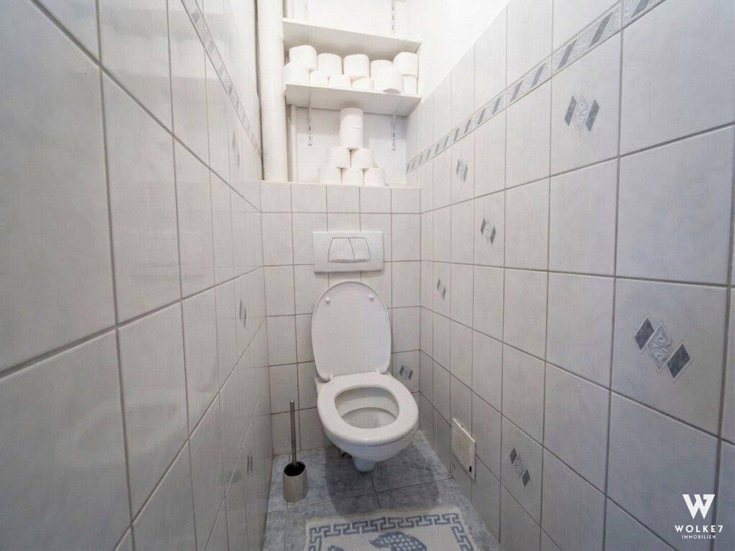 Kleines WC mit Wand-WC und hellen Fliesen an den Wänden.
