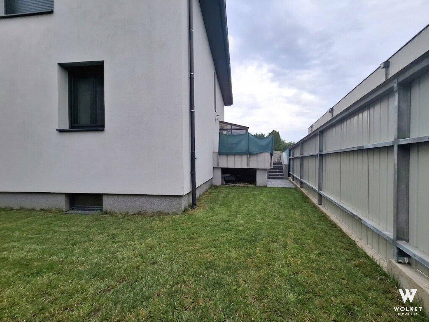 Seitenansicht des Hauses mit schmalem Rasenstreifen und seitlichem Zaun.