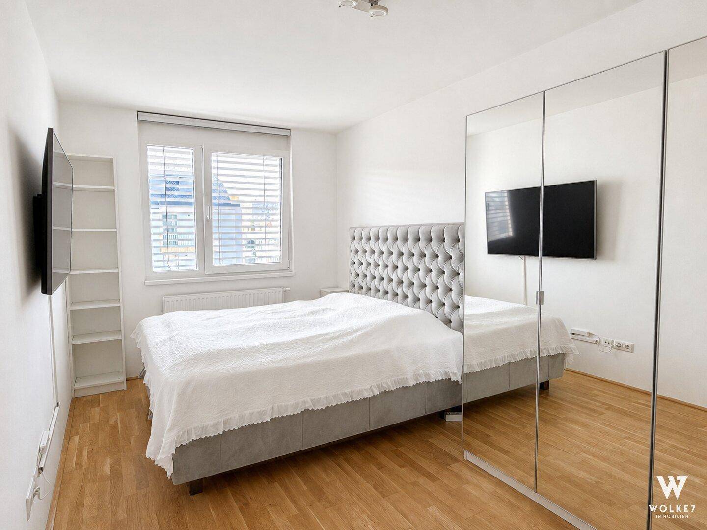 Helles Schlafzimmer mit Holzboden, großem Bett und Spiegelschränken.