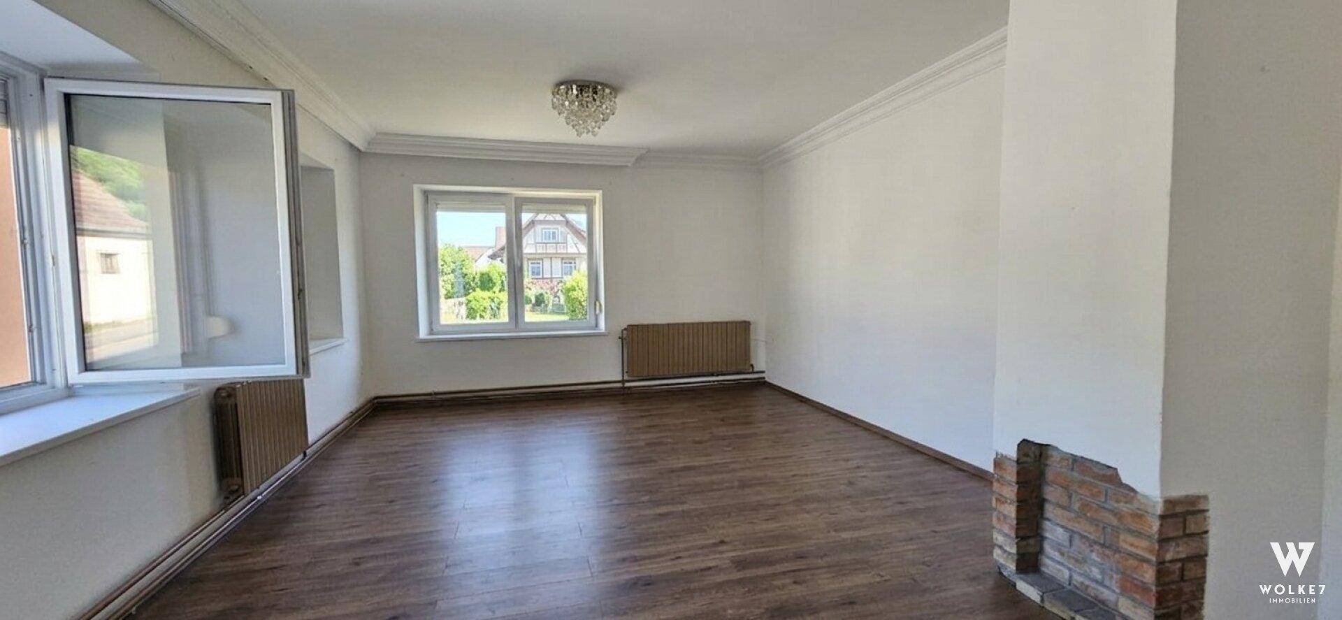 Geräumiges Wohnzimmer mit Holzboden, Stuckdecke und einem Kaminanschluss.