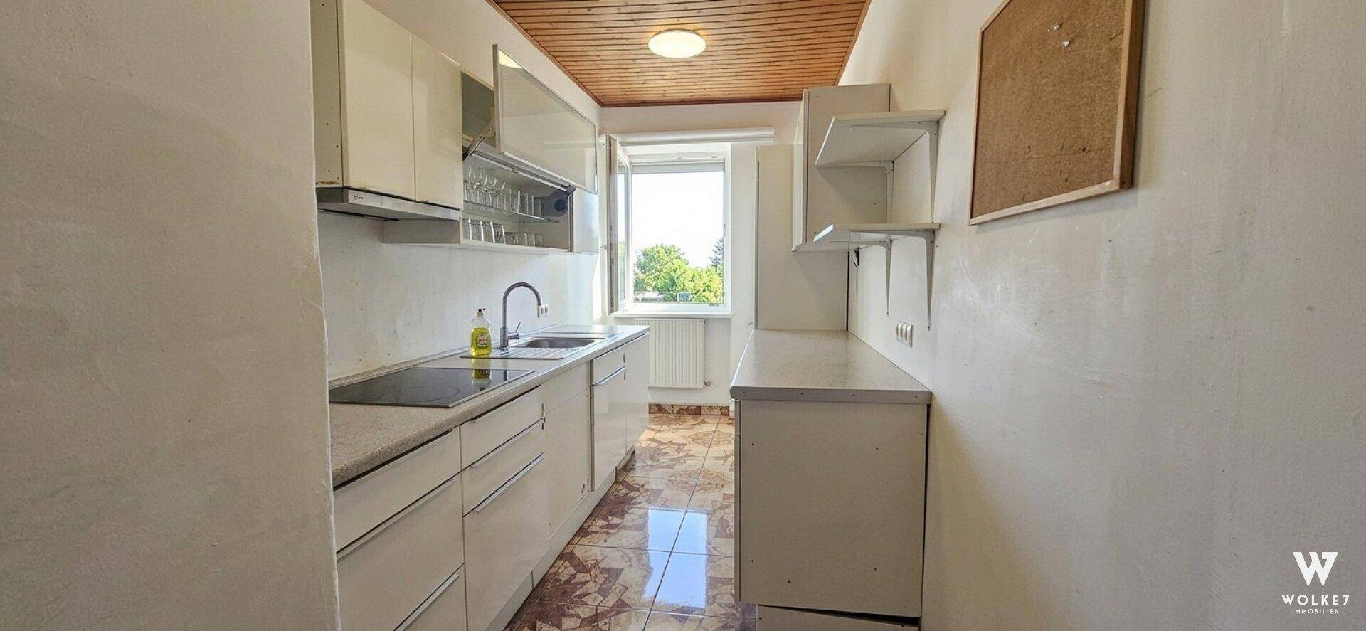Helle Küche mit Holzdecke, weißen Schränken und Fenster mit Blick ins Grüne.