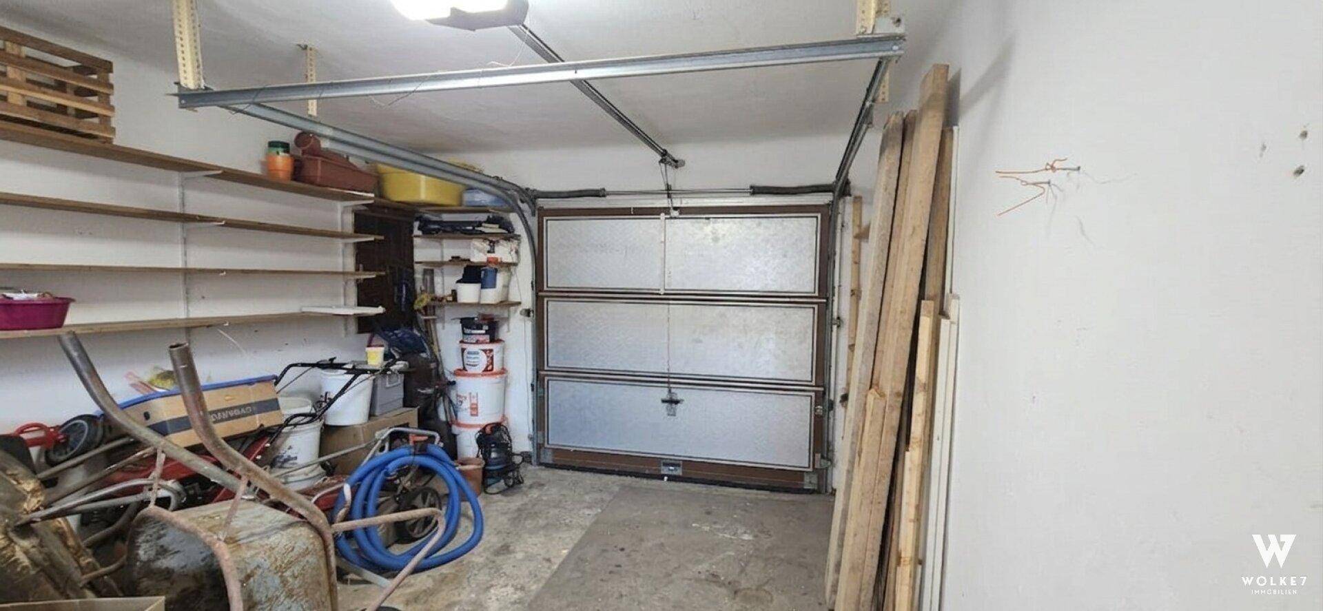 Geräumige Garage mit Rolltor und Regalen für Lagerzwecke und Werkzeuge.