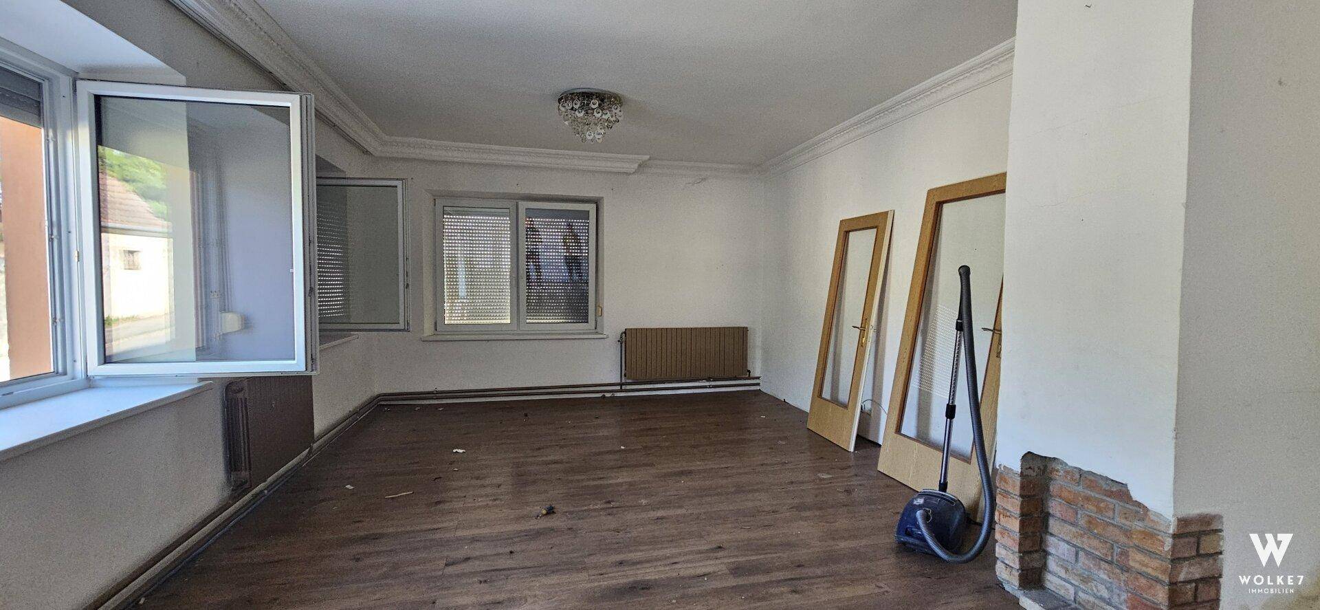 Geräumiges Wohnzimmer mit Holzboden, Stuckdecke und Kaminanschluss, bereit für Renovierung.