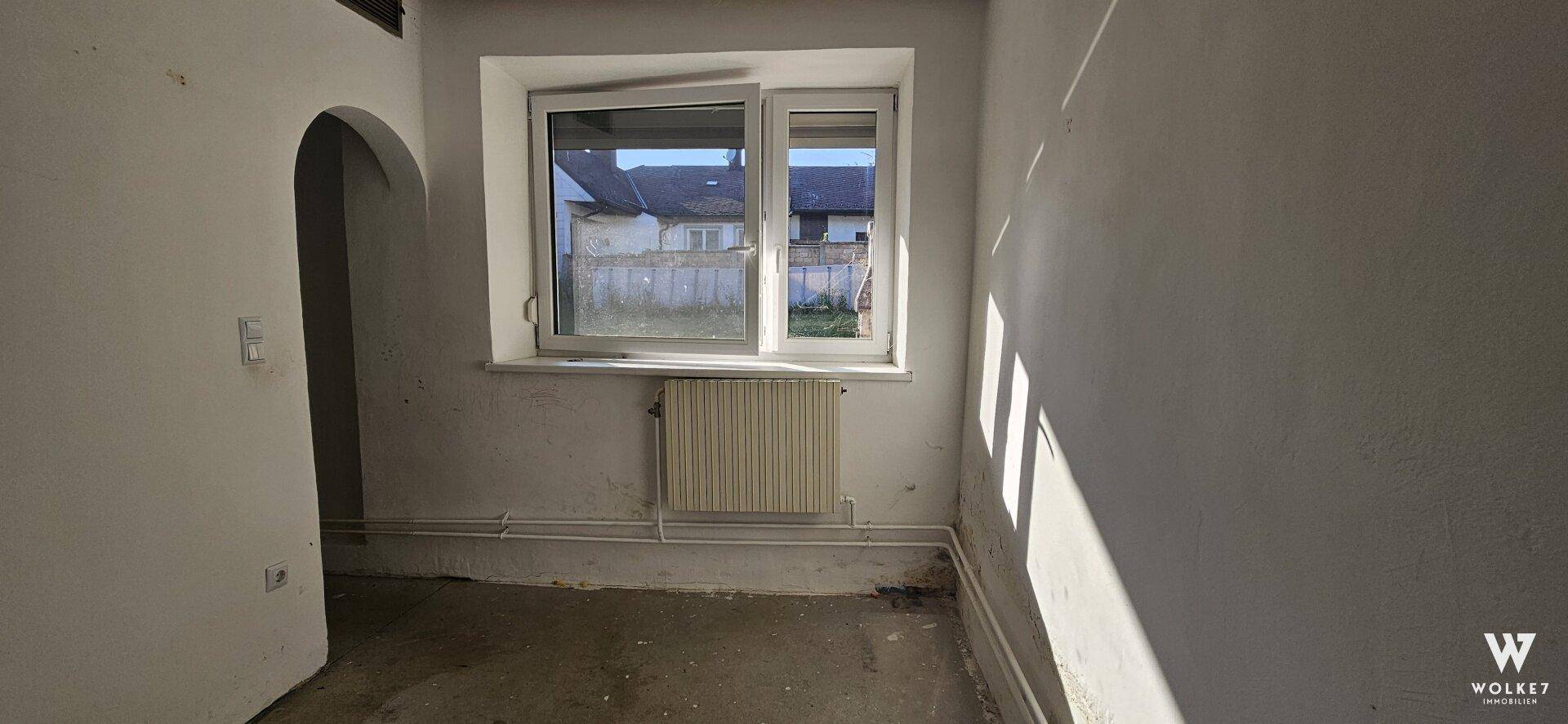 Kleiner Raum mit Fenster, Heizkörper und Bogenöffnung, möglicherweise ein Abstellraum.