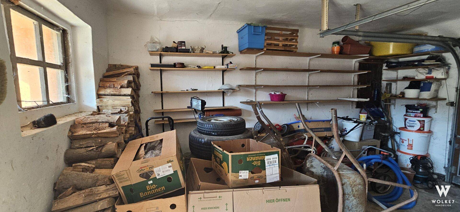 Garage mit Fenster, Holzstapel und Regalen für Werkzeuge und Lagerung.