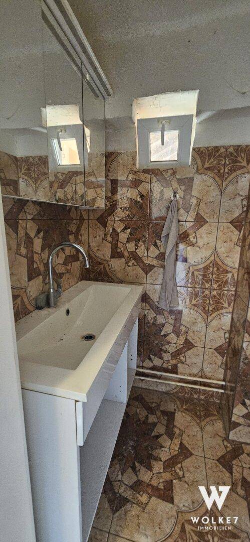 Badezimmer mit gemusterten Fliesen, Einzelwaschbecken und Spiegelschrank.